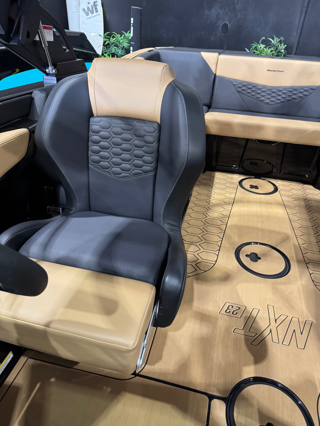 A luxury boat cabin interior featuring a black and tan leather captain's seat with a honeycomb-patterned center backrest, a matching tan and black console bench, and a wood-look floor mat with 'NXT23' branding.
