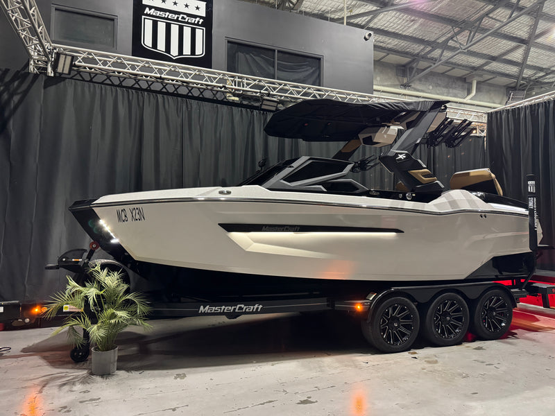 2027 MasterCraft X23 — white hull, tower and trailer against black showroom curtains