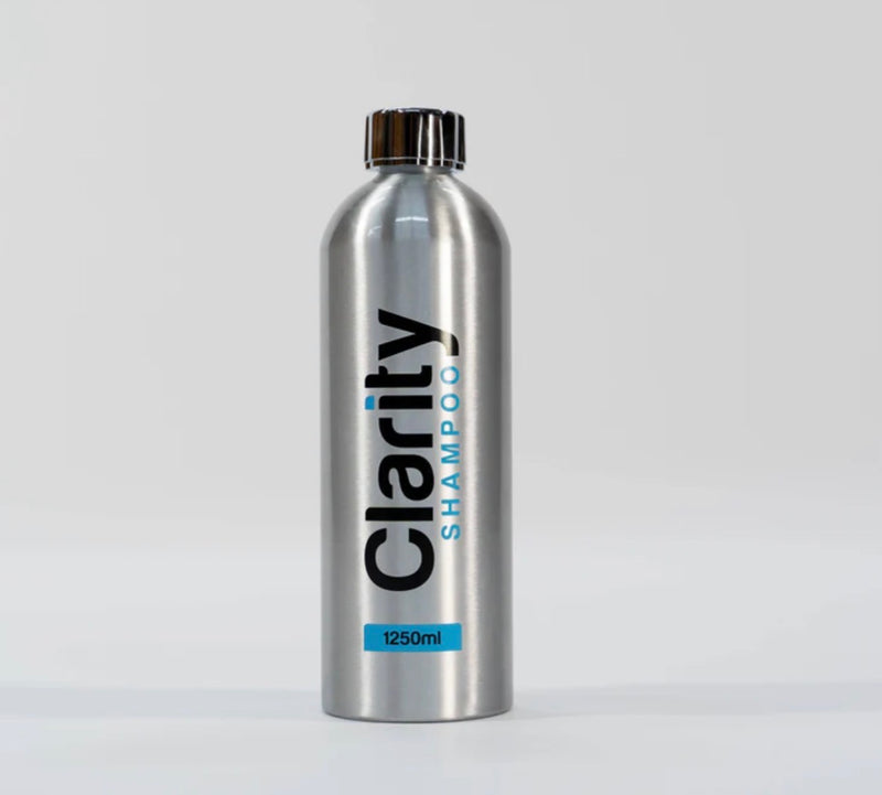 A silver aluminum bottle of Clarity Shampoo with a black ribbed cap, standing upright against a light gray background.