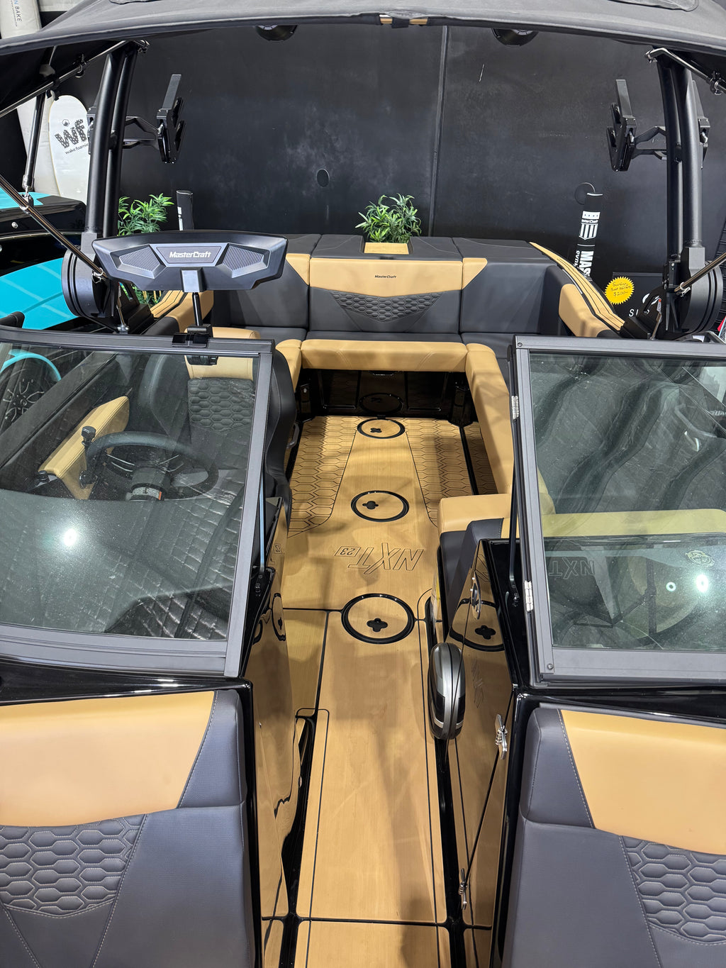 The interior of a luxury boat cabin featuring tan and black upholstery, a central walkway with circular floor mats, a windshield, and a headless dashboard.