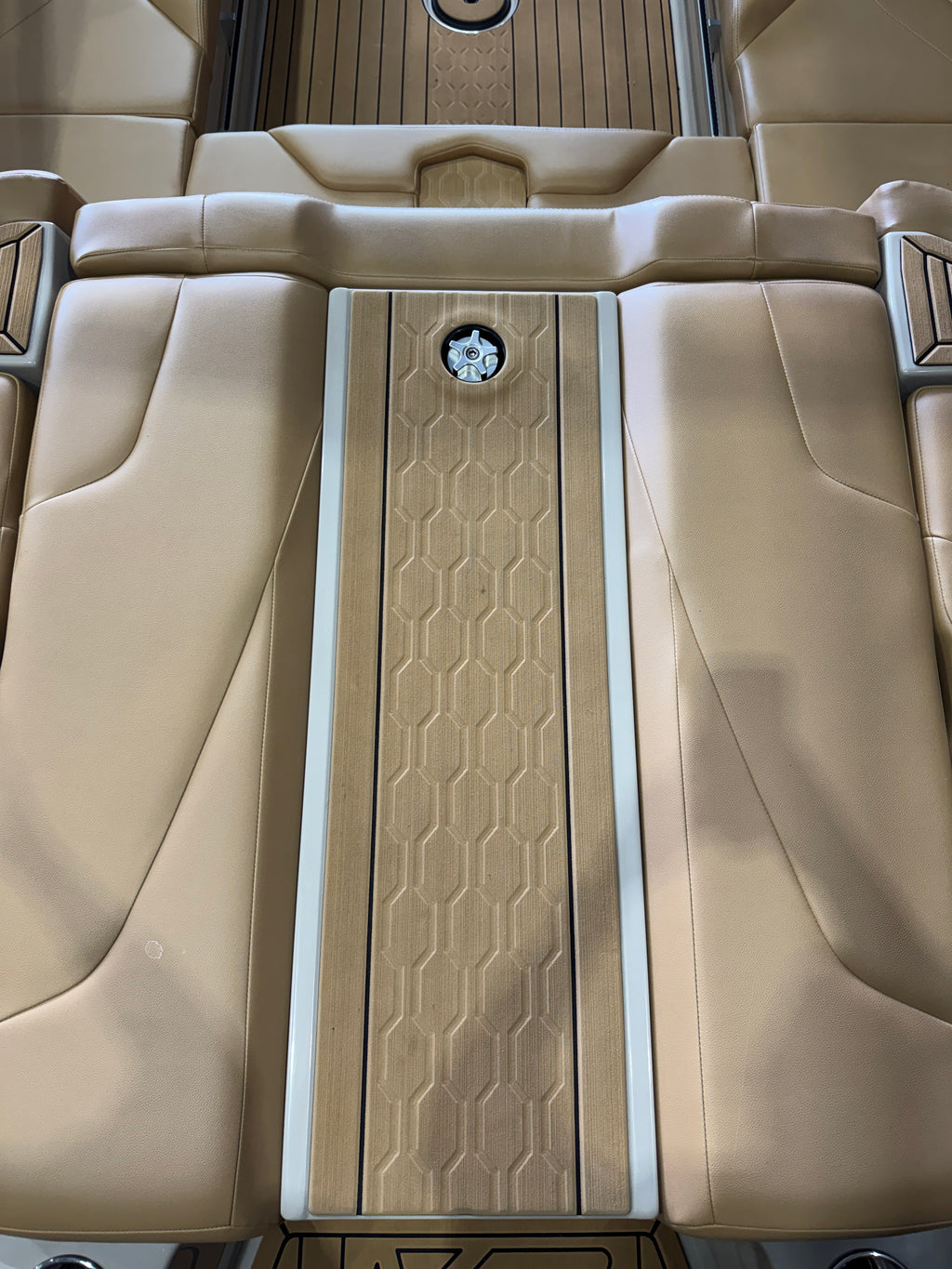 Close-up of a luxury MasterCraft XT22T Boat interior showing beige leather seats and a central wood-look floor console with a honeycomb pattern and a circular emblem.