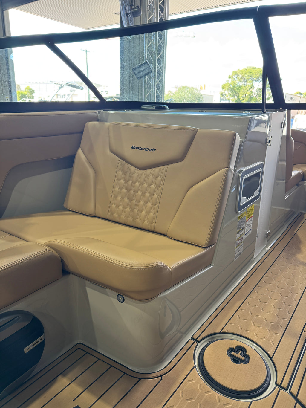 Beige and tan upholstered Mastercraft XT22T boat seating with a tufted backrest cushion, shown inside a boat cabin with wood-look flooring and a windshield.
