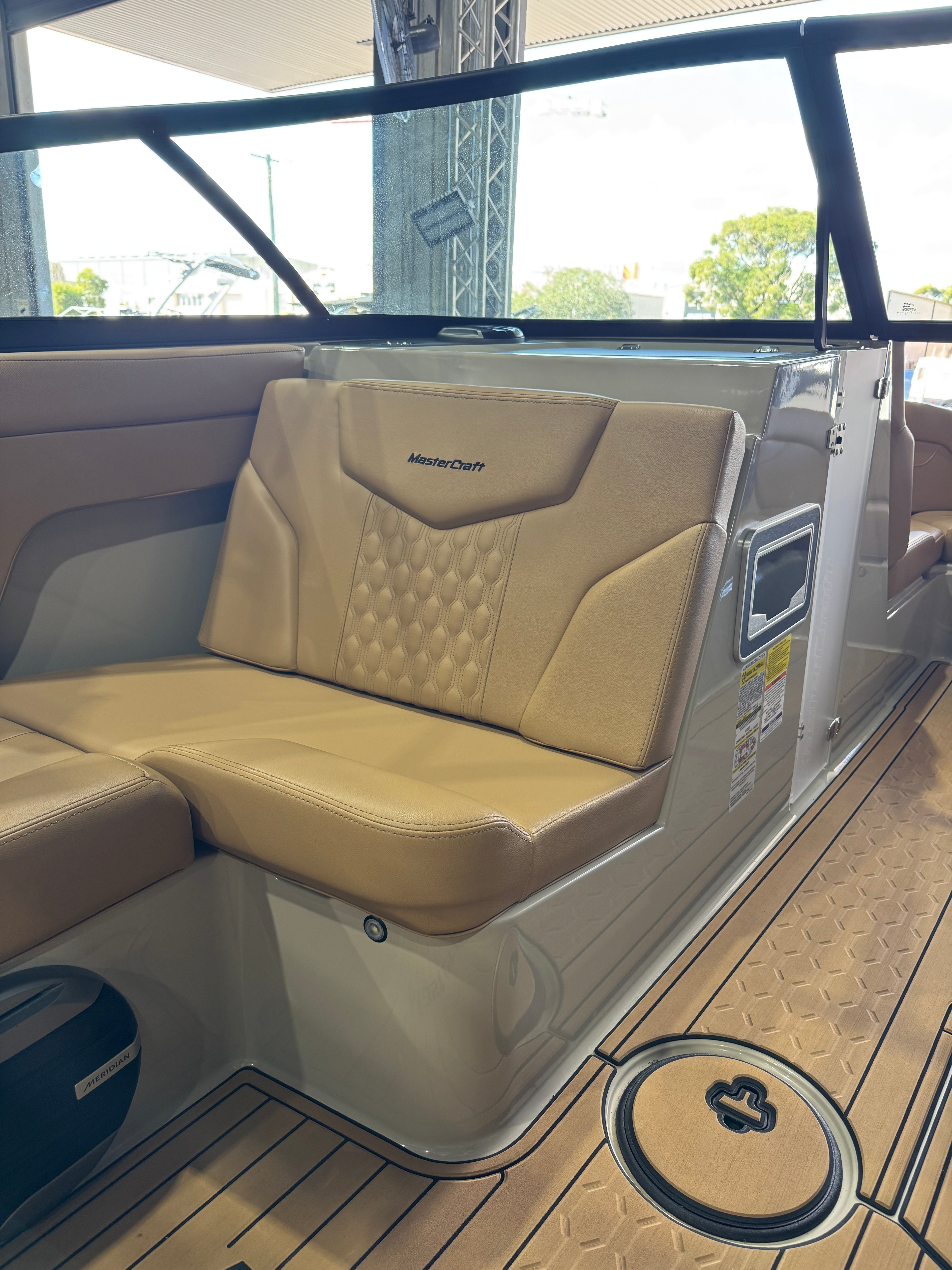 Beige and tan upholstered Mastercraft XT22T boat seating with a tufted backrest cushion, shown inside a boat cabin with wood-look flooring and a windshield.