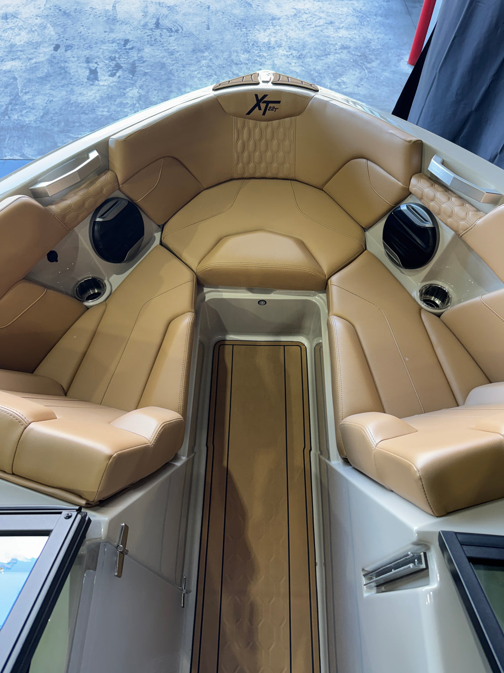 The interior cockpit of a boat featuring tan leather seating, a wood-look floor mat, and a white hull with a visible MasterCraft XT22T logo on the bow .