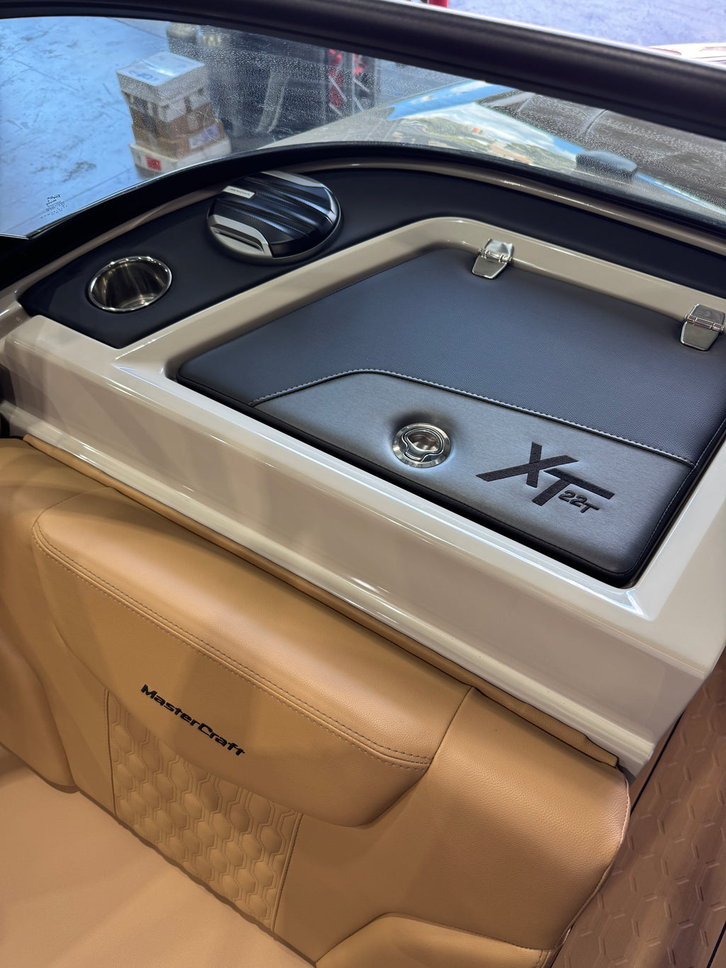 Close-up of a boat cabin interior showing a tan leather MasterCraft seat and a black storage compartment with a white trim and the word 'XT22T' on the lid.