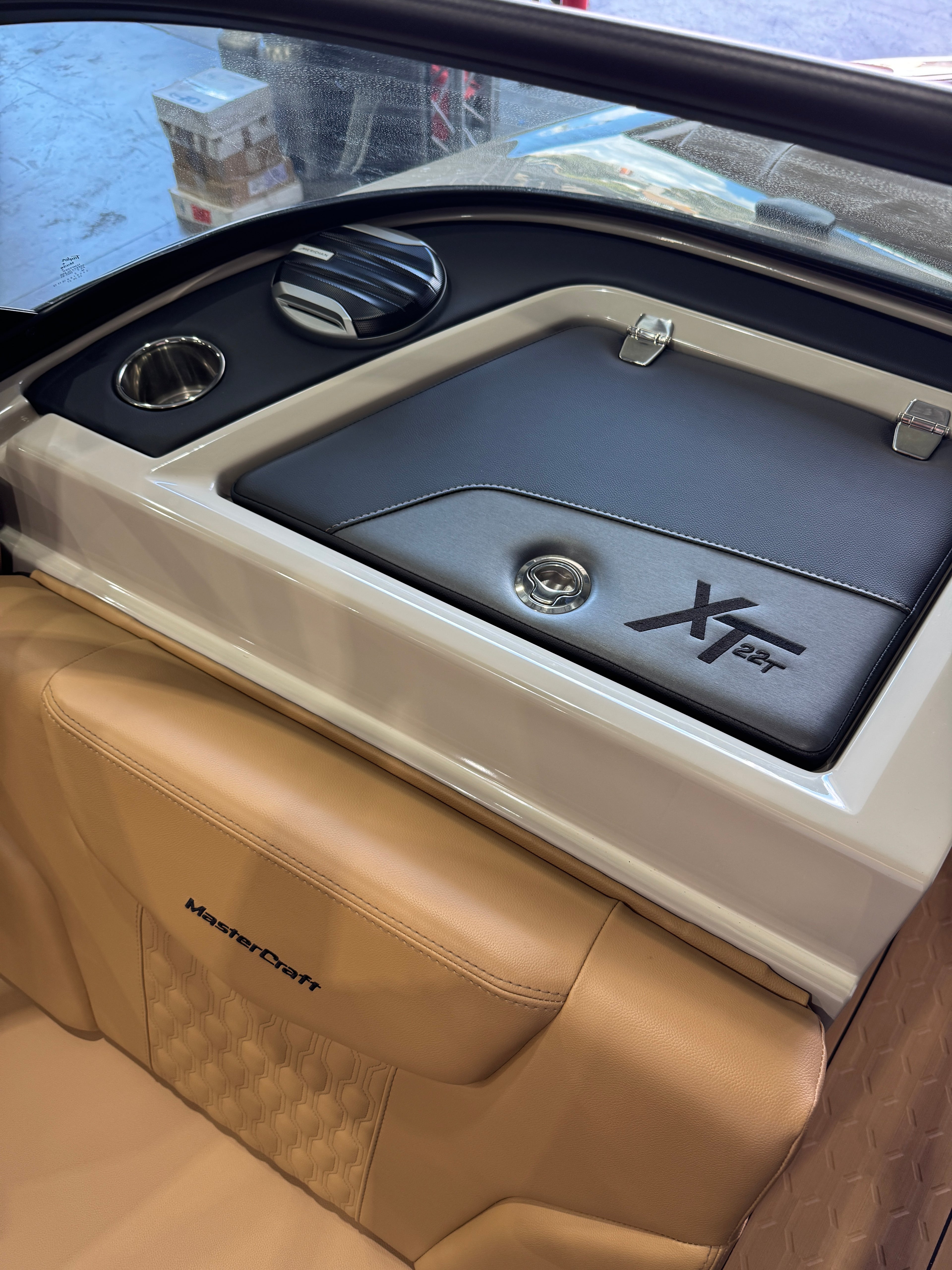 Close-up of a boat cabin interior showing a tan leather MasterCraft seat and a black storage compartment with a white trim and the word 'XT22T' on the lid.