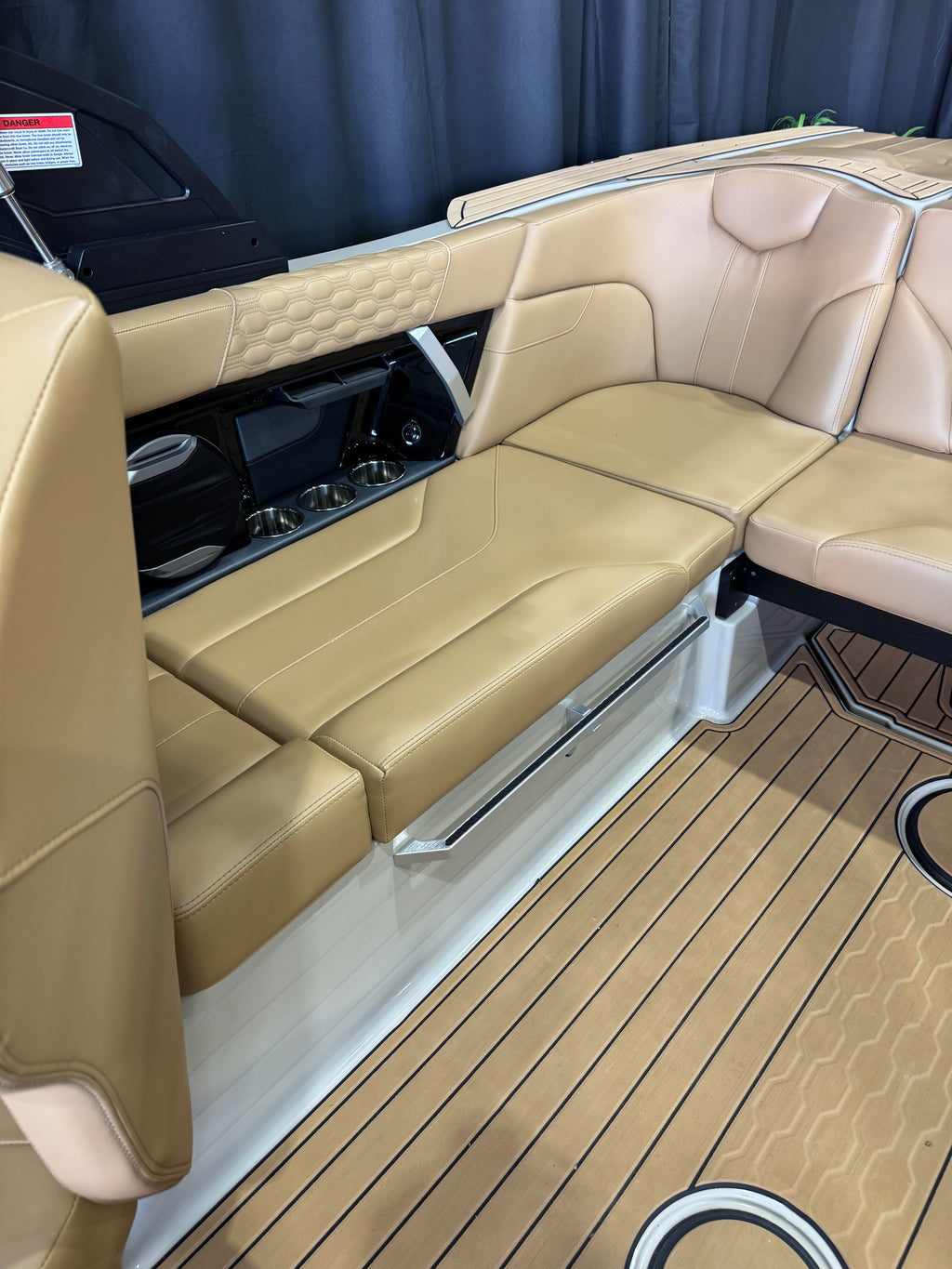 Beige leather boat seating with a fold-down bench and wood-look deck flooring inside a MasterCraft XT22T boat cabin.