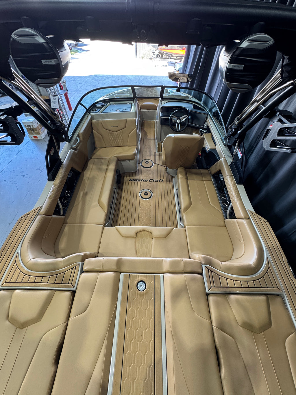Top-down view of a luxury MasterCraft XT22T boat interior with tan leather seating, wood-look flooring, and a windshield, photographed in a showroom 