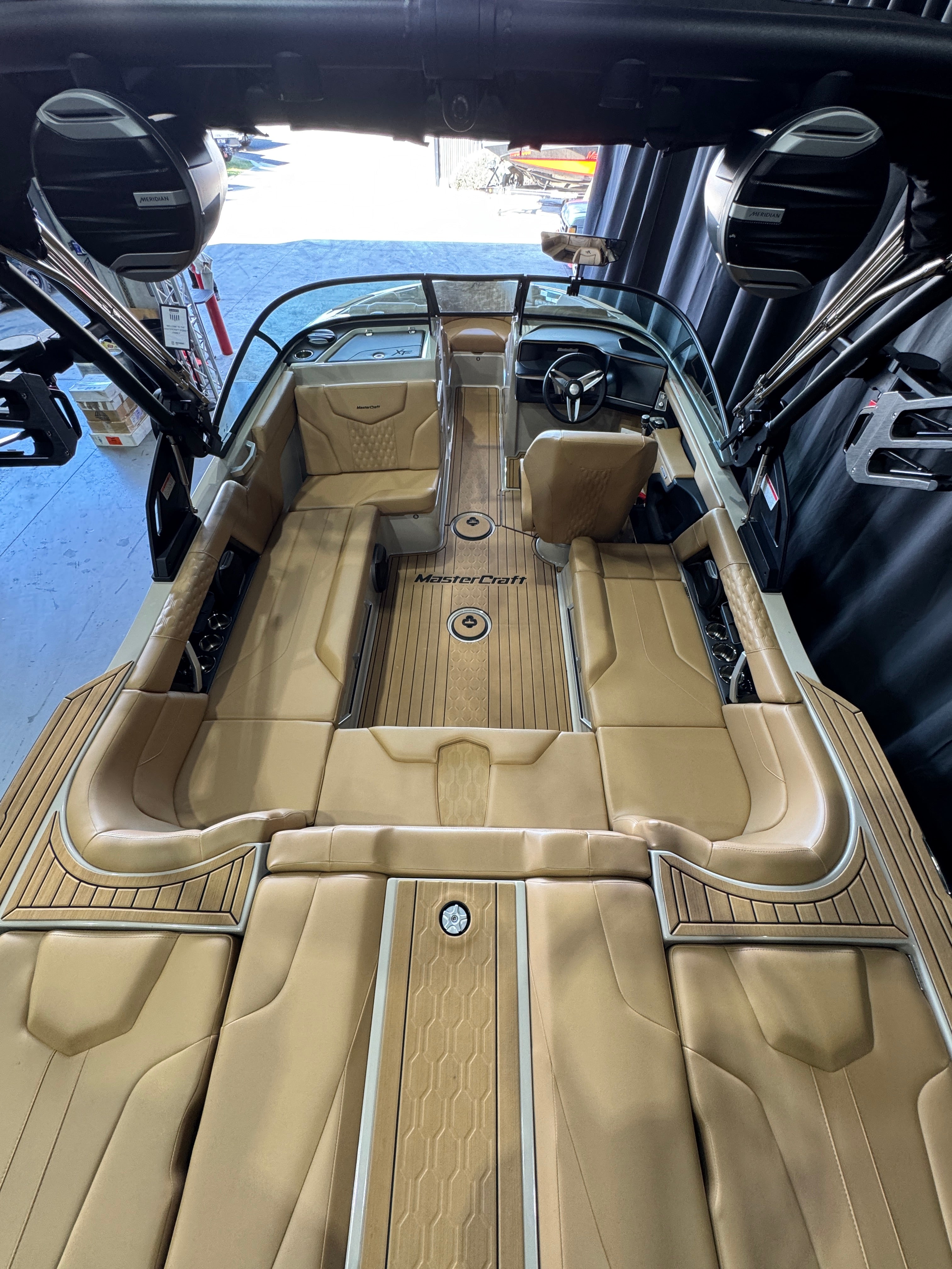 Top-down view of a luxury MasterCraft XT22T boat interior with tan leather seating, wood-look flooring, and a windshield, photographed in a showroom 