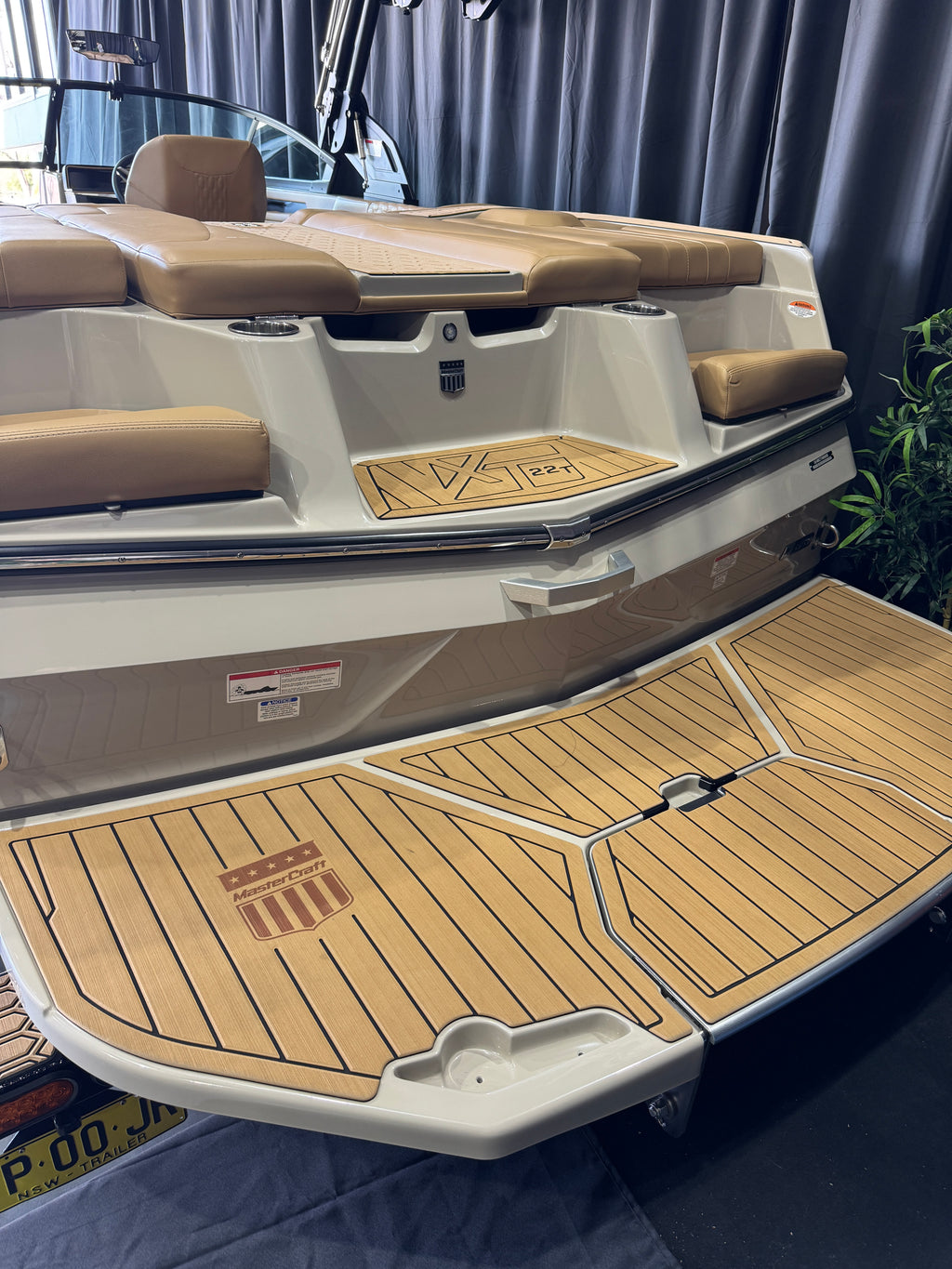 A close-up of the stern and lower deck of a boat with tan cushioned seating, tan teak-look flooring, and a fold-down wooden boarding platform MasterCraft XT22T