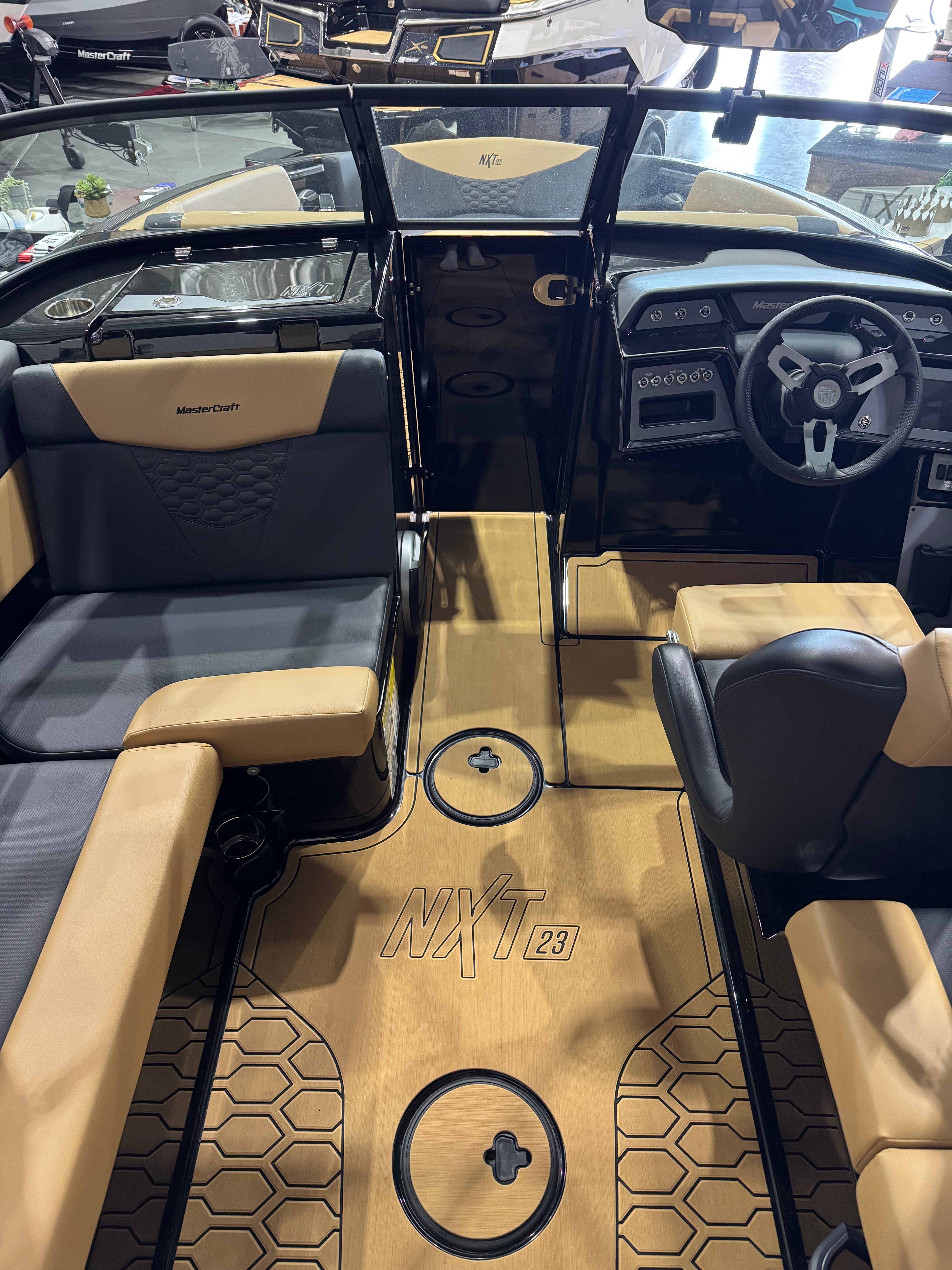 The interior of a boat cabin with tan and black upholstery, a black steering wheel, and a wood-look floor featuring the model name 'NXT 23'.