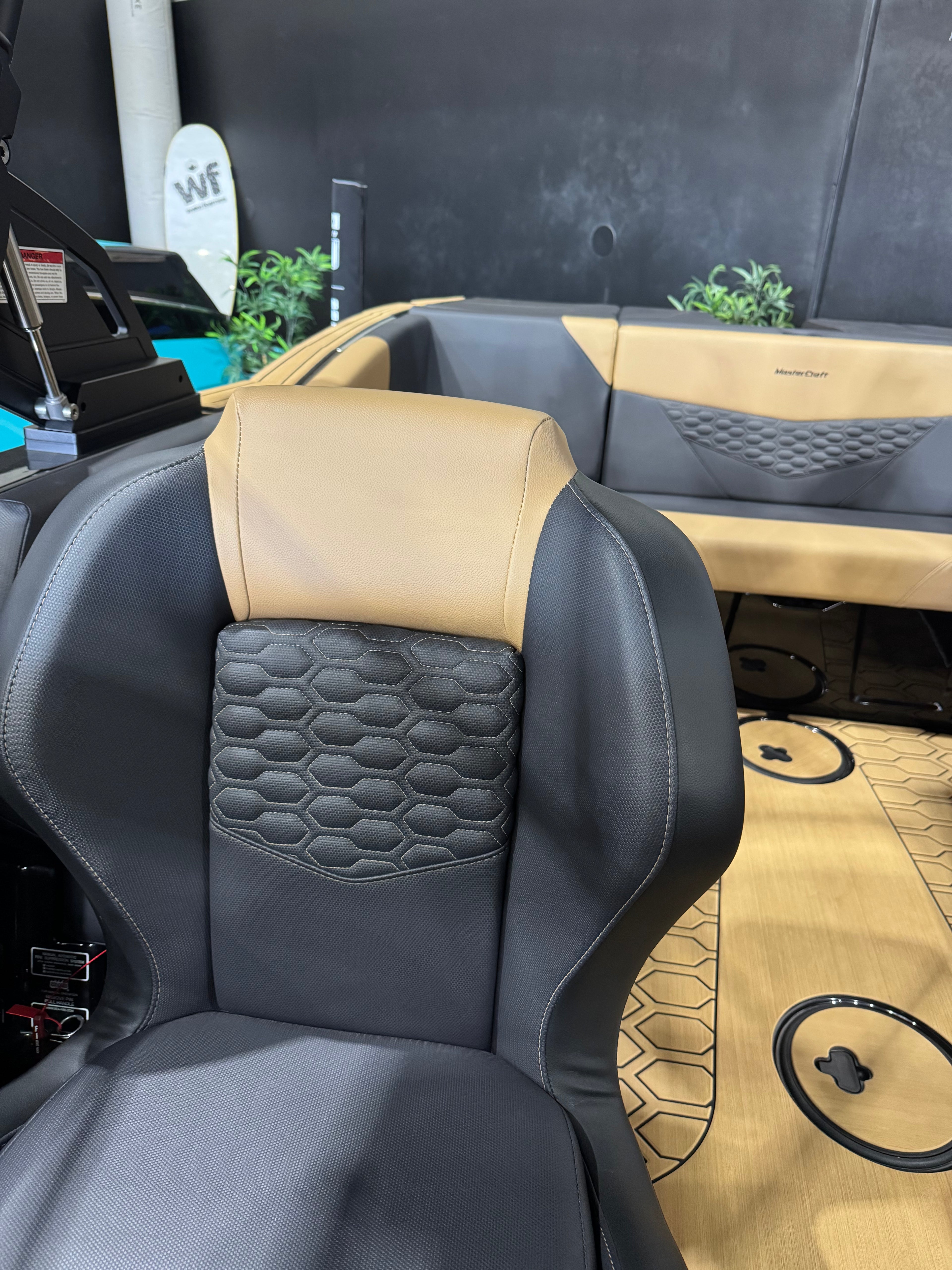 A close-up of a luxury boat interior seat upholstered in black and tan leather, featuring a honeycomb quilted pattern on the backrest. A matching tan and black bench seat is visible in the background along with a patterned wood-look floor mat.