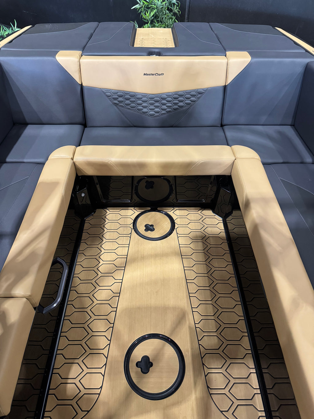 Close-up of a boat seating area with dark blue upholstered cushions and tan leather-like trim, showing a patterned tan floor mat with circular black details.