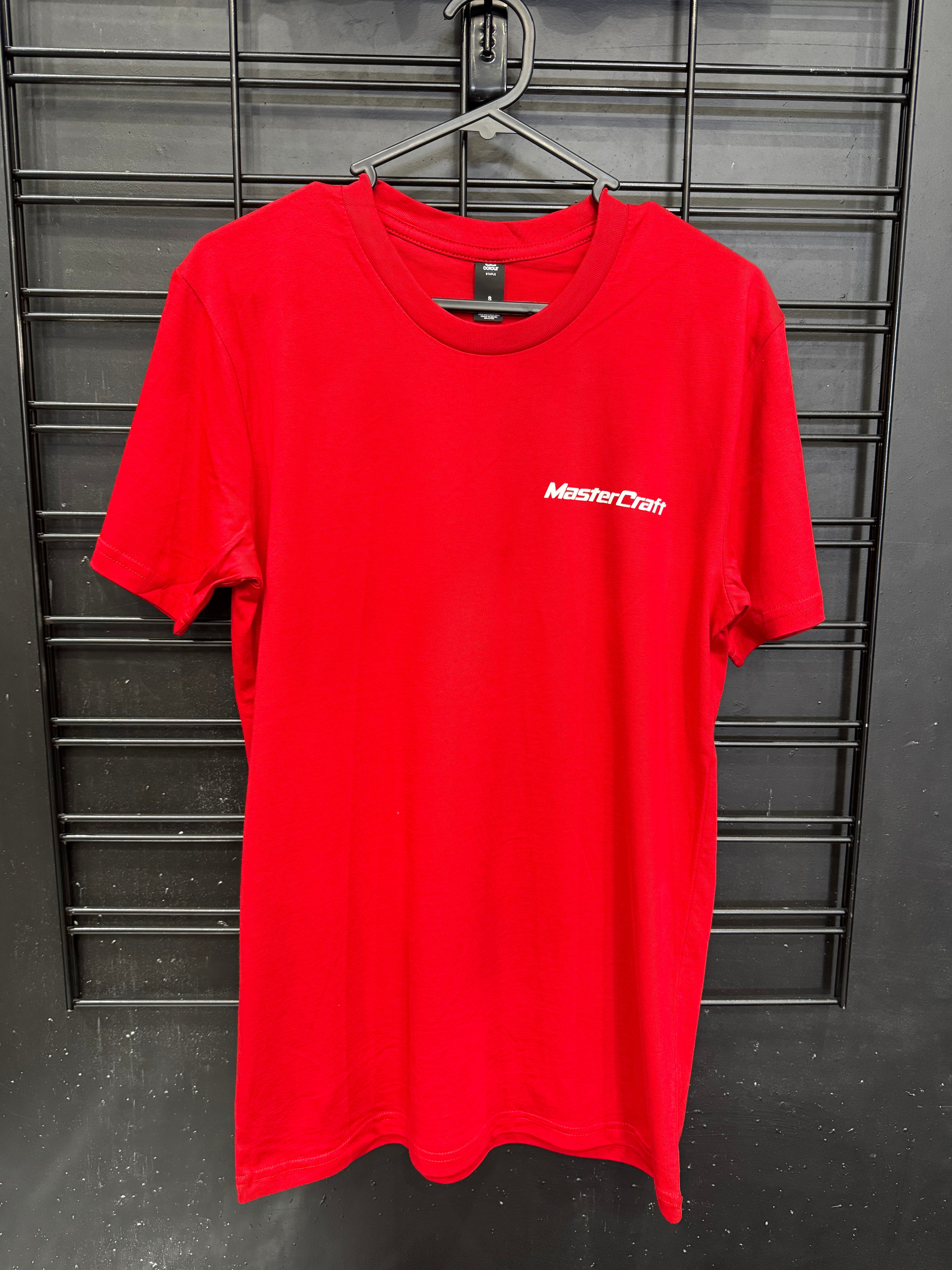 A bright red short-sleeve crewneck t-shirt hanging on a black wire hanger against a black metal grid wall. The shirt features the 'MasterCraft' brand logo printed in white on the left chest.