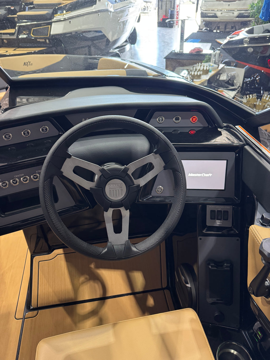 The helm station of a boat with a black steering wheel, digital instrument display, and tan leather seats.